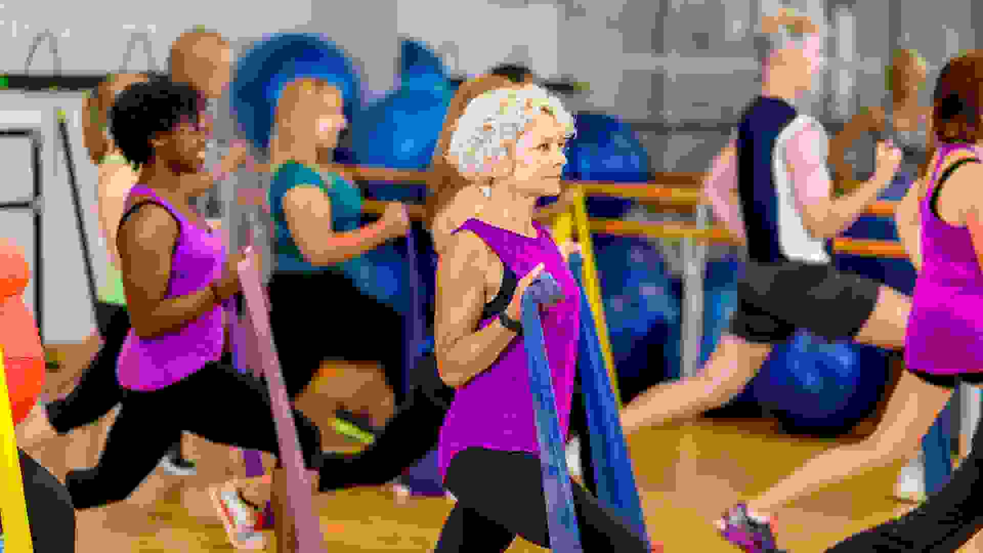 A multi-aged and multi-ethnic group of adults using elastic bands to help their strength training workout in a fitness class at a community complex.