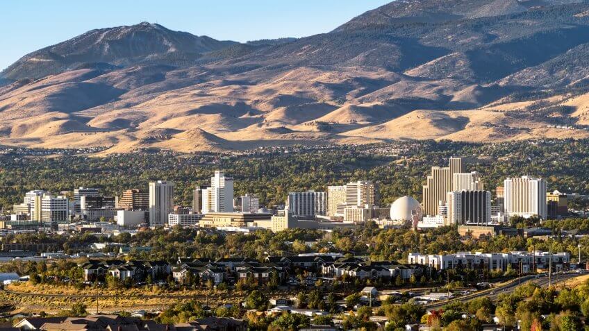 City of Reno Nevada cityscape in early autumn with hotels, casinos, apartments and mountains in the background.