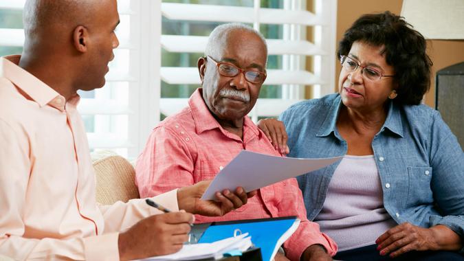 Financial Advisor Talking To Senior Couple At Home Showing Documents.