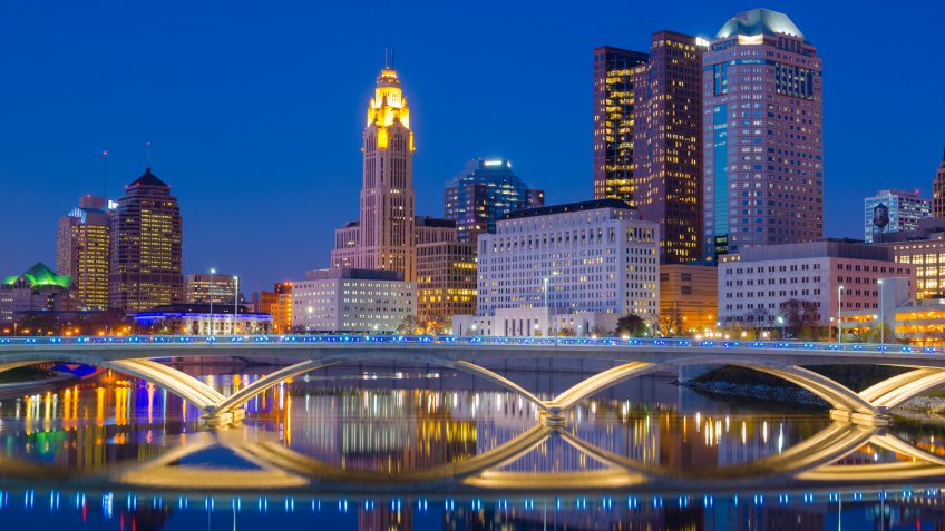 Downtown Columbus skyline at late dusk / early evening with a partial skyline reflection off of the Scioto River.
