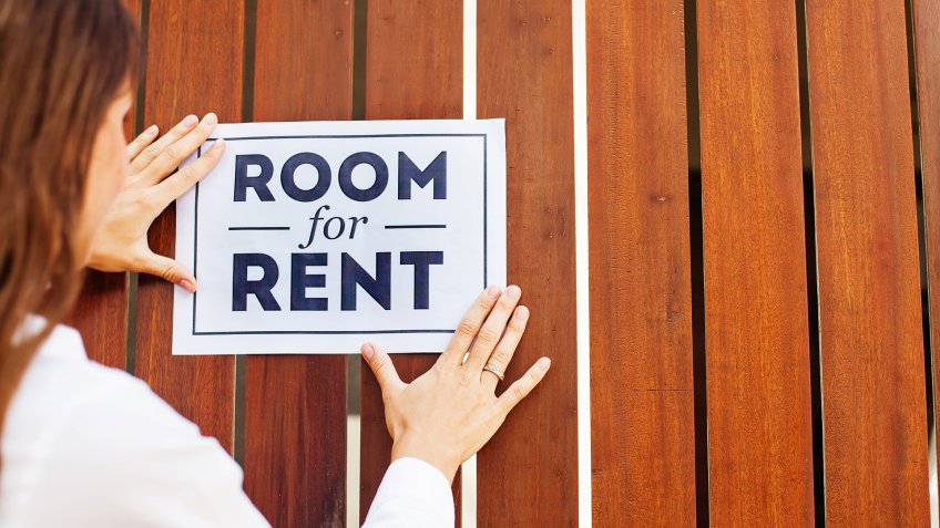 woman attaching a "room for rent" ads on a wooden wall.