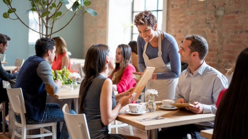 Friendly waitress serving couple at a restaurant taking orders and looking very happy.