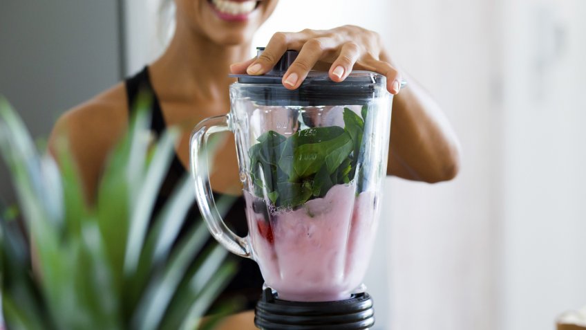 Woman blending spinach, berries, bananas and almond milk to make a healthy green smoothie.