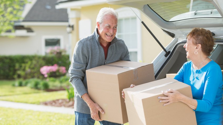 A happy senior couple moving boxes into or out of the back of their car.