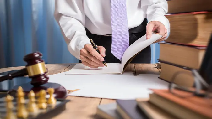 An image of an unidentifiable lawyer signing papers at a desk with books and a gavel in front of them.