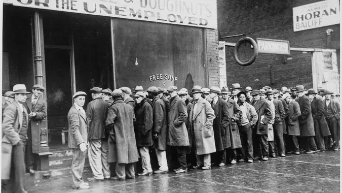 A black and white image featuring a line of unemployed people during the Great Depression.