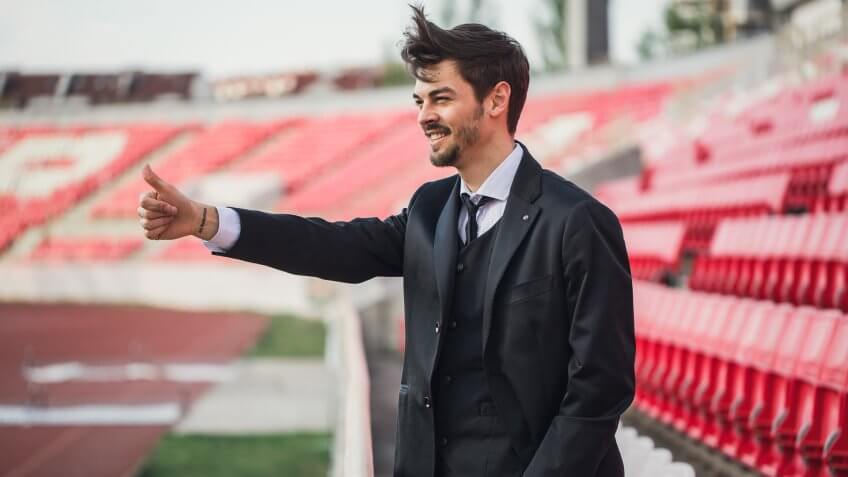 Manager man standing on stadium grandstand and showing thumbs up.