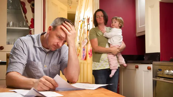 Man stresses over his bill while his wife and child stand in the background.