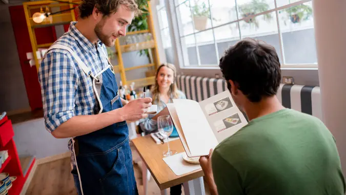 Waiter working at a restaurant and taking an order to a couple of young people.