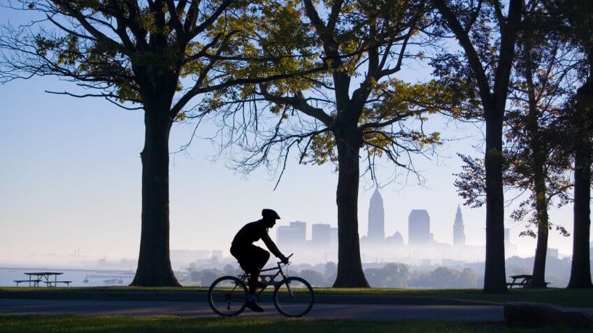 Silhouette of biker riding in park with trees and Cleveland skyline in background on a foggy morning.