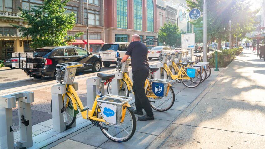 Man parks and locks bicycle at a bike sharing station in downtown Indianapolis, Indiana, USA on a sunny day.