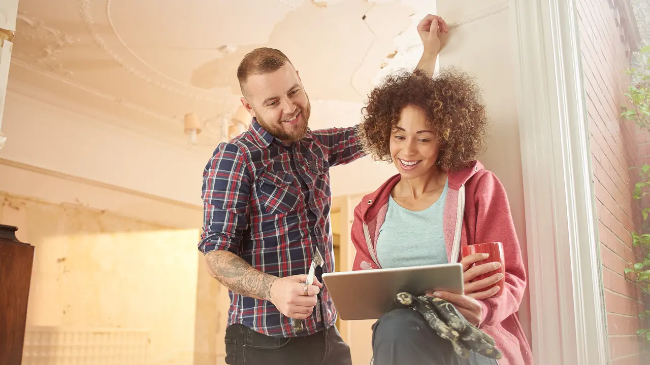 a young couple take time out from scraping walls in her new house to check for great deals on their digital tablet.