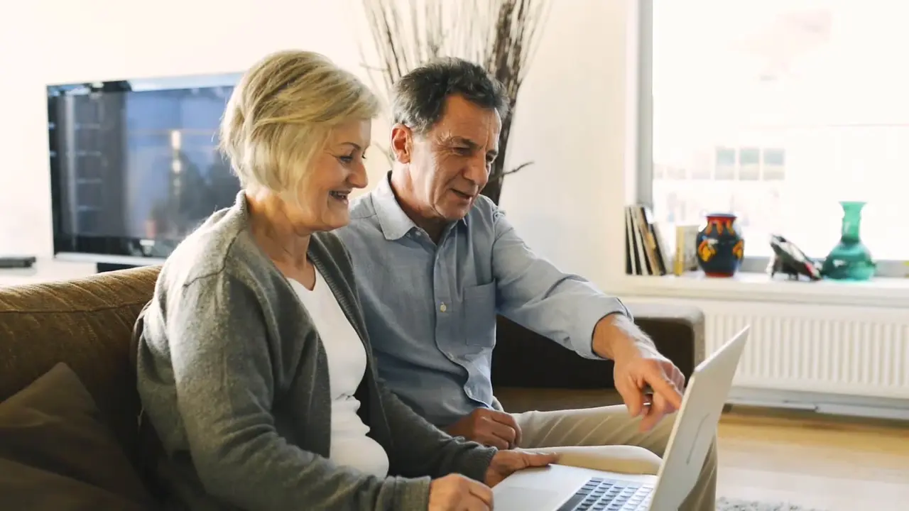 A couple sitting on a couch looking over financials on a laptop.