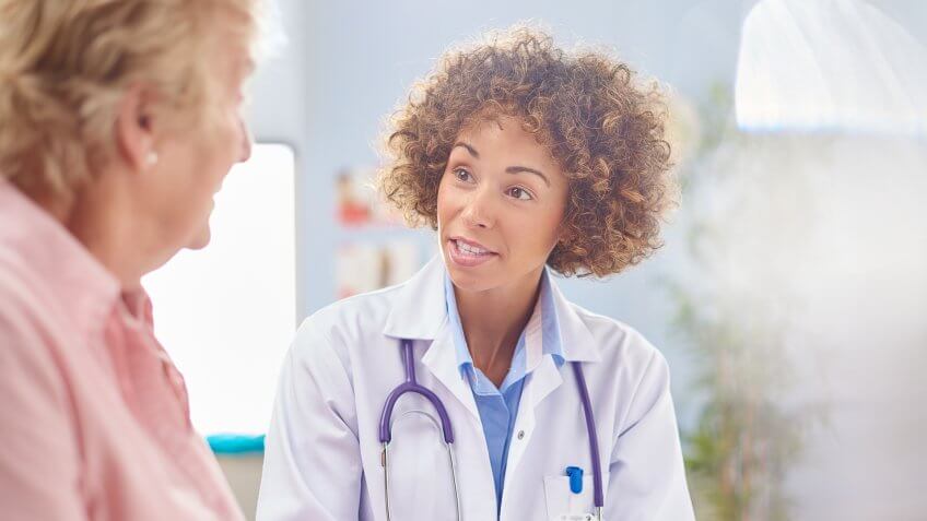 a female doctor sits and listens to a senior woman sitting down in a consultation room .