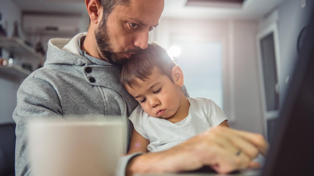 Father working on laptop at home office and holding son on his lap.