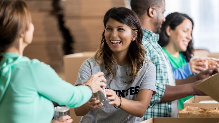 Cheerful mid adult Hispanic female volunteer accepts a canned food donation during community food drive.