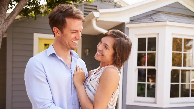 A happy Caucasian couple holding each other in front of a brand new home stock photo