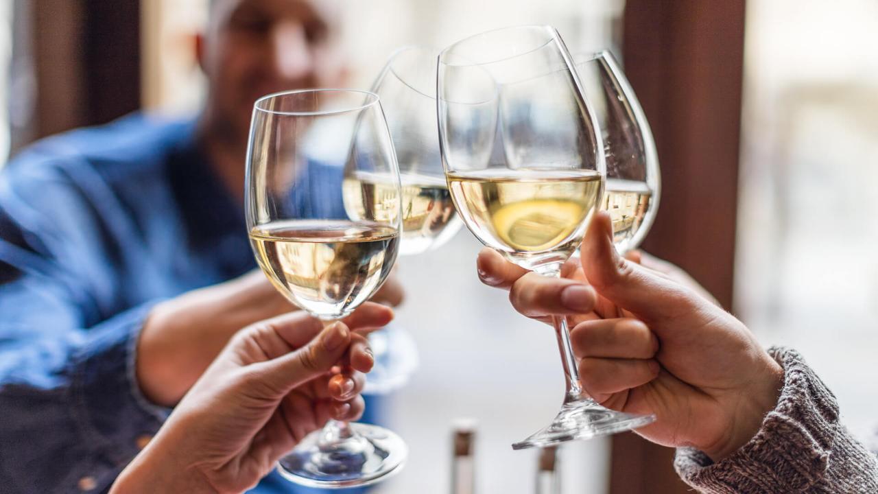 Friends toasting each other with white wine, smiling, sitting in restaurant.