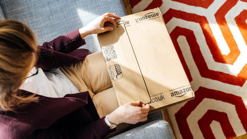 PARIS, FRANCE - APR 24 2017: Living room view from above of woman unpacking unboxing Amazon cardboard box logotype printed cardboard box side.