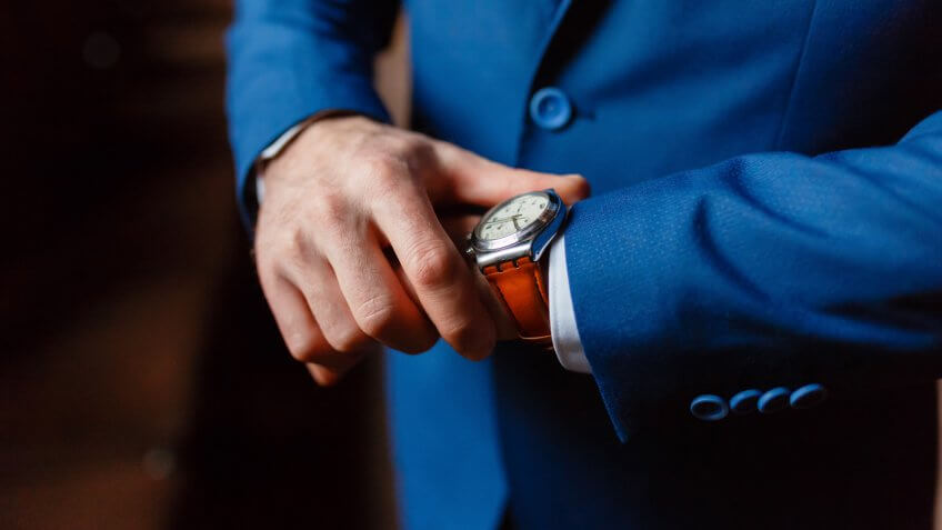 Closeup with businessman hands closing elegant blue suit jacket and wearing banker expensive wrist watch.