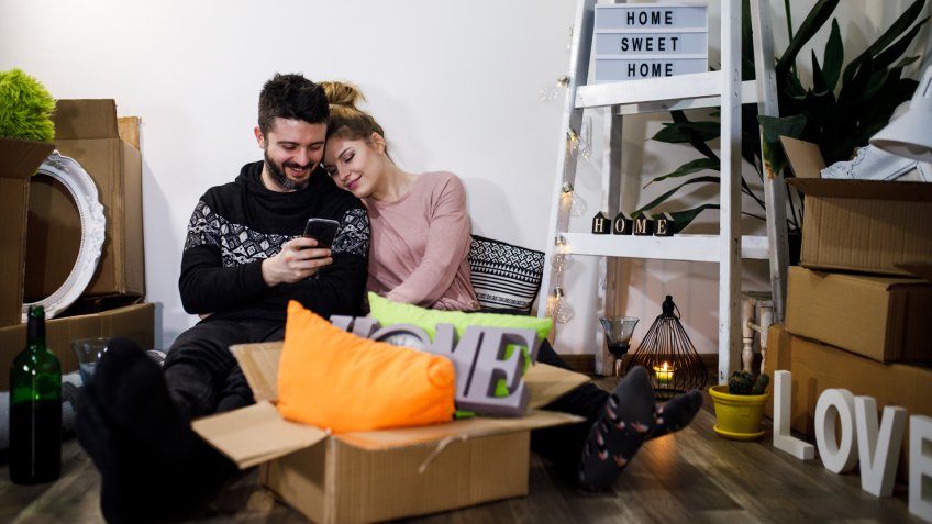 young couple using mobile phone in their new home