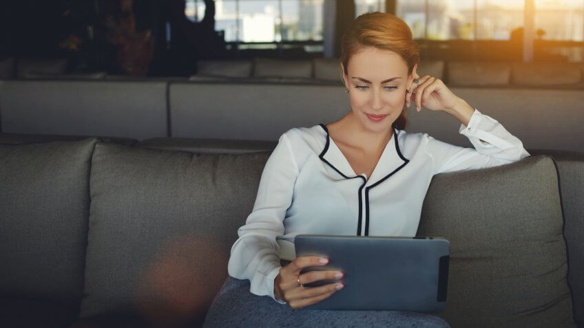 woman reading electronic book via internet on digital tablet while relaxing in coffee shop after work day, modern female watching fashion news on touch pad while waiting order in cafe.