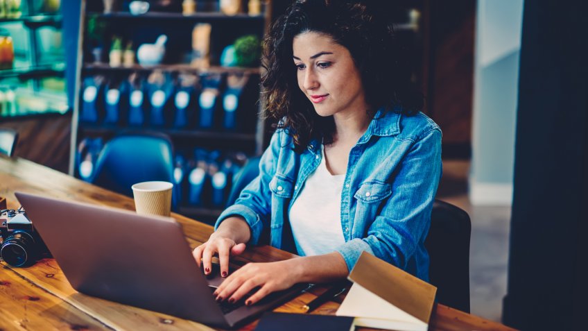 Young beautiful woman dressed in stylish outfit transferring money using online banking service on laptop computer connected to wifi.