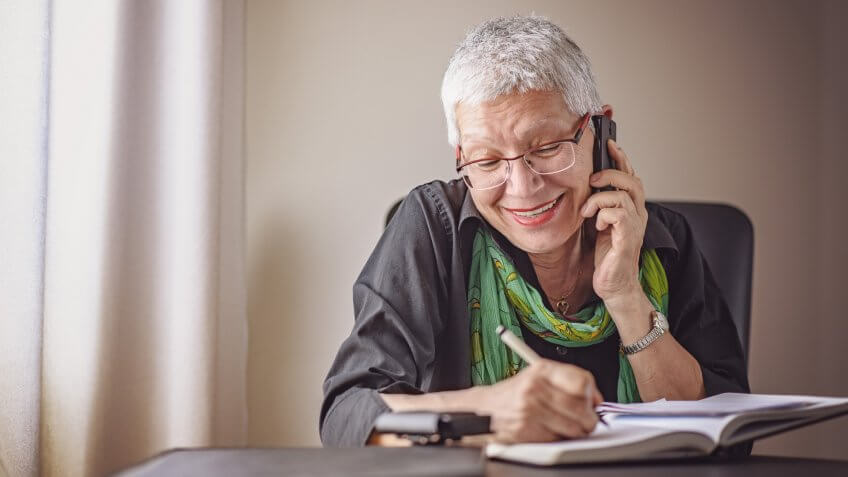 senior business woman writing down orders, talking on her cell phone.