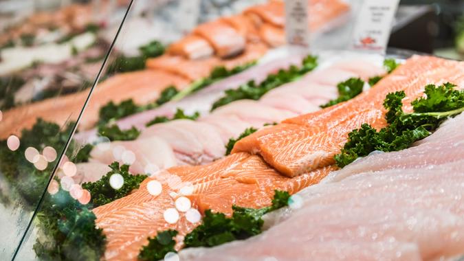 Seafood stand with cuts and filets of salmon and tuna on ice behind glass.