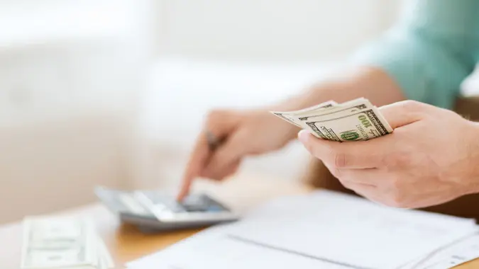 savings, finances, economy and home concept - close up of man with calculator counting money and making notes at home.