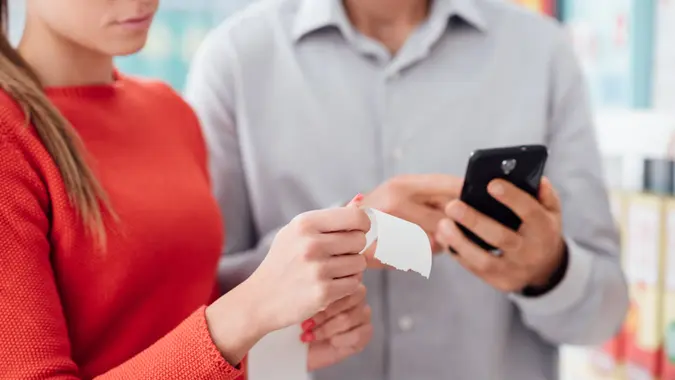 Couple doing grocery shopping at the supermarket they are checking a long receipt and using apps on the phone.