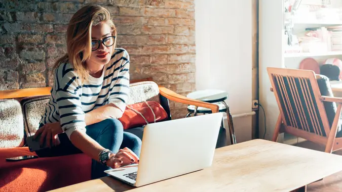 Young blonde female student using portable laptop computer while sitting in a vintage coffee shop.
