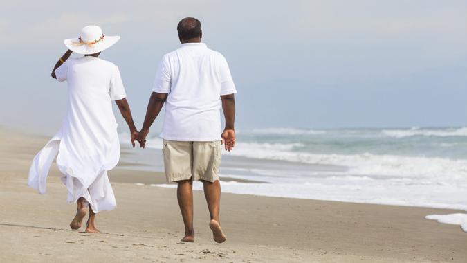 Happy romantic senior African American man and woman couple walking holding hands on a deserted tropical beach.