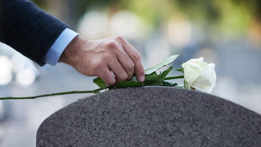 man placing a white rose on a grave