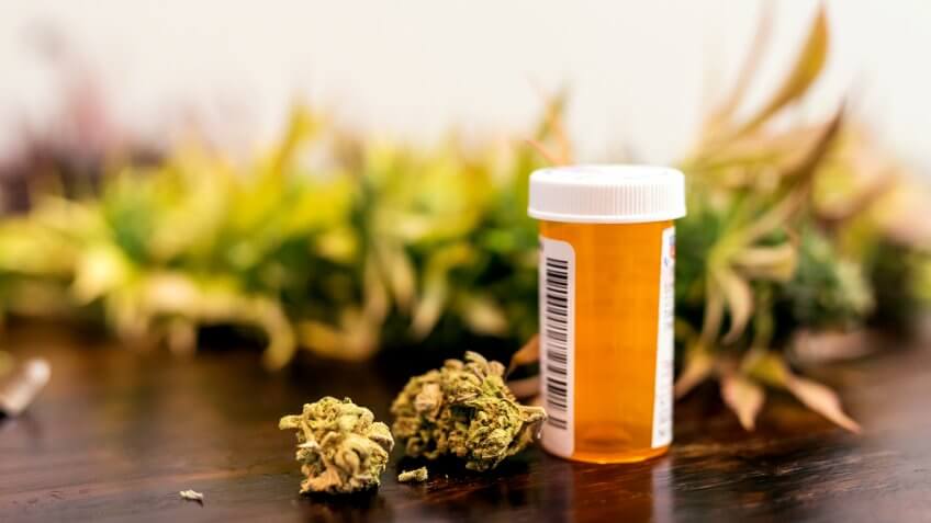 Marijuana buds sitting next to prescription medicine bottle.