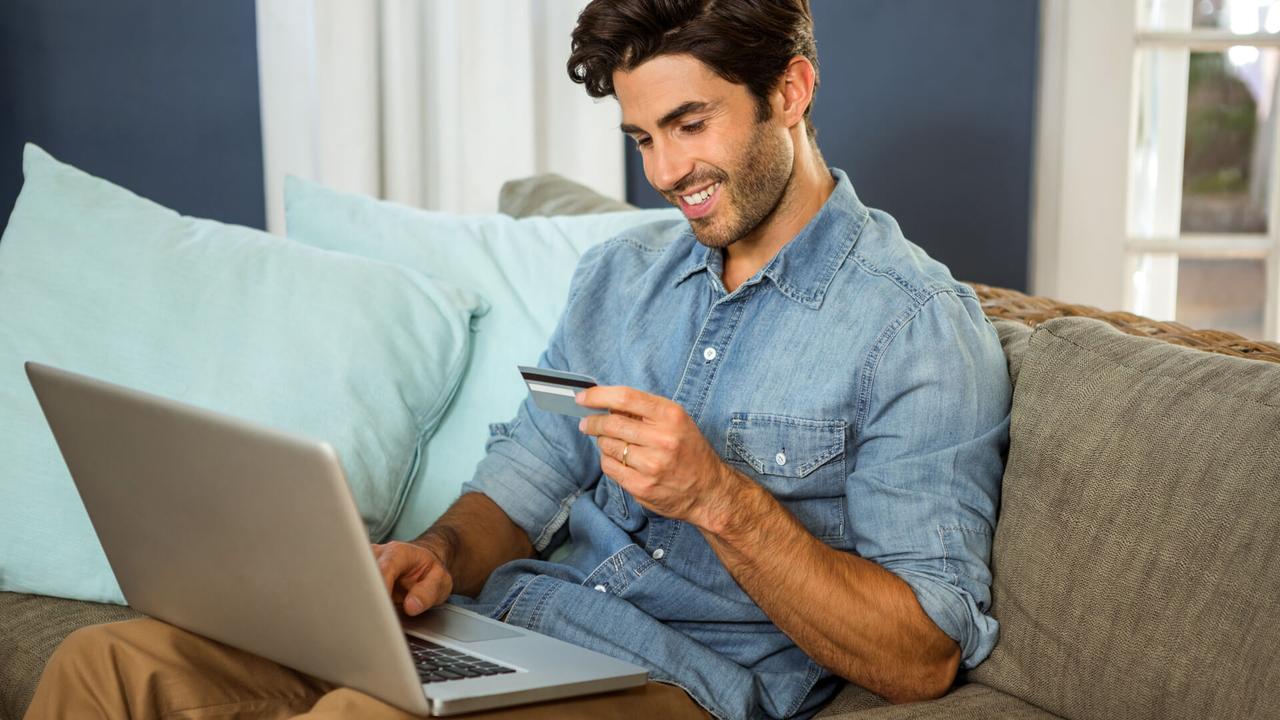 happy man on sofa looking at credit card with laptop