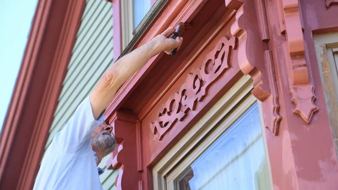 An older man in an historic town paints his house