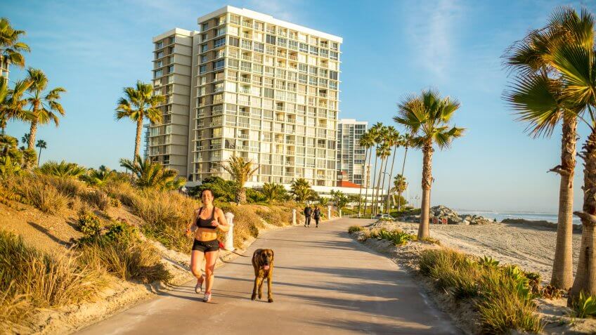 Coronado, USA - January 14, 2016: Woman with dog running on Coronado Island Beach, USA.