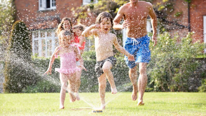 Family Running Through Garden Sprinkler