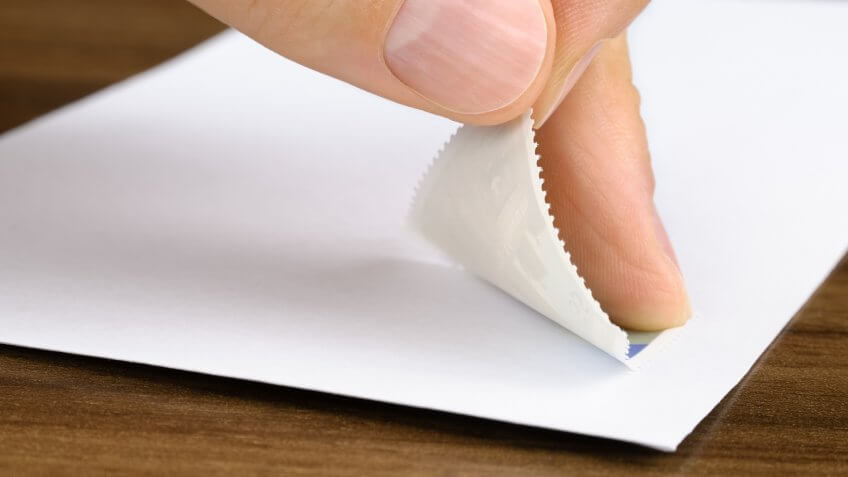 Studio closeup of a hand pasting a stamp onto a white envelope.