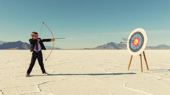 A young boy dressed in business suit, glasses and tie holds shoots a bow and arrow towards a target on the Bonneville Salt Flats in Utah.