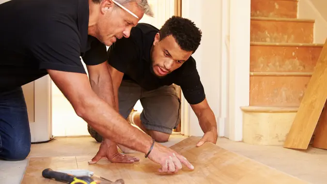 Two men laying wood panel flooring in a house.
