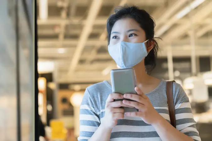 new normal after covid19 epidemic smart asian female wear protection mask hand use smartphone communication in department store new lifestyle abstract blur background.