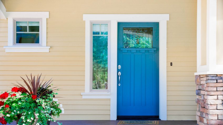 A front entrance of a home with a blue door, yellow siding, and a flowerpot in daytime.