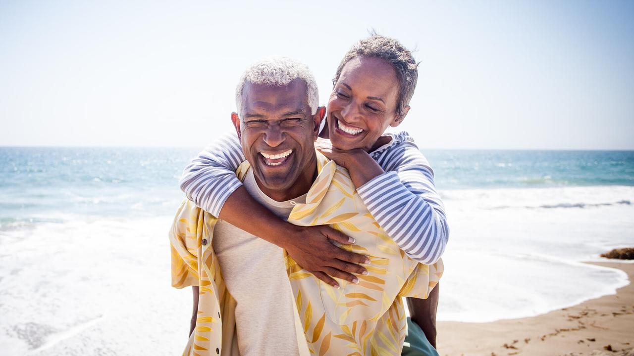 A beautiful senior black couple piggyback on the beach.
