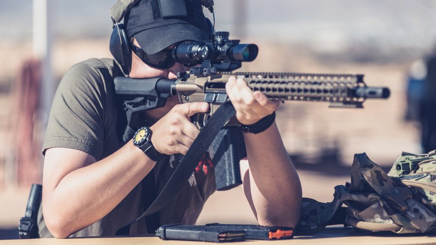 Man shooting assault style rifle at shooting range in desert resting on bench front - Image.