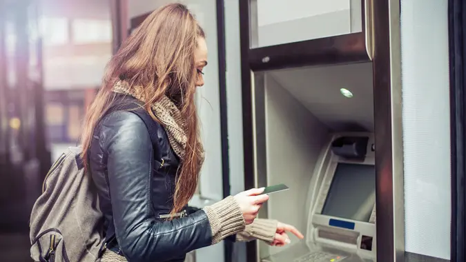Young woman withdrawing money from credit card at ATM,, fees, America, money, payment, avoid fees, bills, debt
