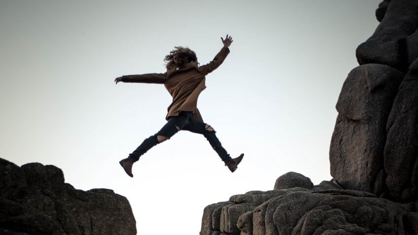 Woman taking a risk by jumping between two cliffs