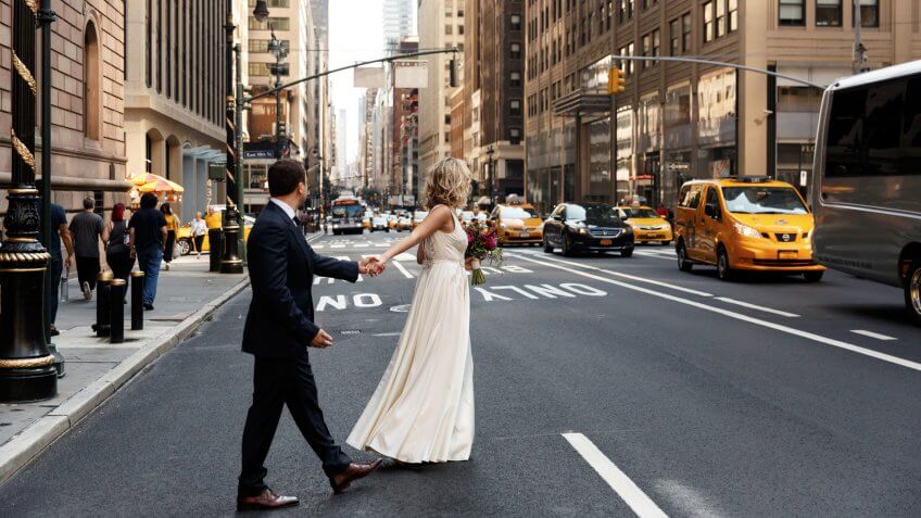 Bride holds groom's hand walking across the street in New York.