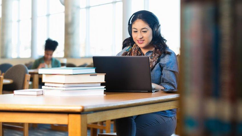 Stock, shares, NASDAQ, S&P 500, money, Young adult Hispanic woman is studying in college library.
